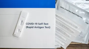 A box reading COVID-19 Self-Test (Rapid Antigen Test) surrounded by swabs from the kit
