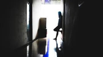 Stock photo of a lonely woman in shadow standing at the end of a dark corridor