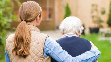 A woman walks with her arm around her older mother as they enjoy spending time together.