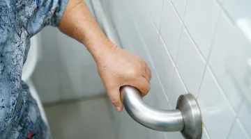 A close up of the hand of an older woman holding on the a grab bar in her bathroom for prevent falling