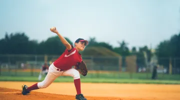 A young boy wearing a red uniform throws a pitch from the pitcher's mound at a youth baseball game