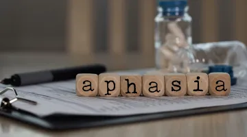 A series of wooden letters spelling out the word APHASIA with a pen and medicine bottle in the background