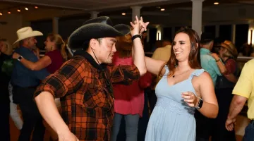 A man in a cowboy hat and plaid shirt dances with a woman at South Shore Health's 2022 Kickin' Up Country event.