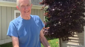 An older gentleman smiling while pushing a lawn mower