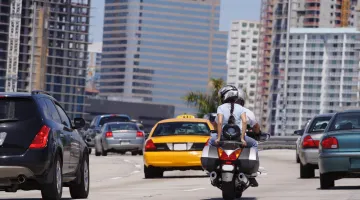 Two riders on a motorcycle on a the highway, with other cars around them in normal traffic.