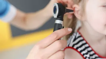 A close up view of a doctor looking in a young child's ear for a suspected ear infection