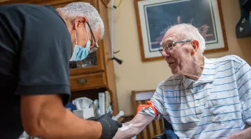 A male MIH paramedic administers IV medication to an elderly patient