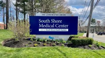 The exterior sign at South Shore Medical Center Norwell, featuring green shrubs, tulips, and other colorful spring foliage