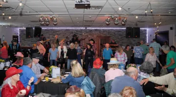 A panoramic view of the crowd at Kickin' Up Country 2023, featuring people line dancing and seated wearing western-themed attire.
