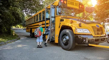 Two children wait in line to get on a school bus as it stops on a suburban street